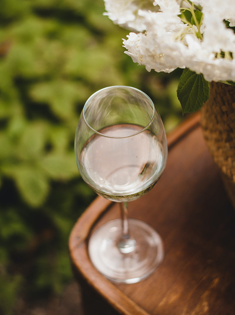Ein Glas lieblicher Weißwein steht auf einem kleinen Tisch neben weißen Blumen.